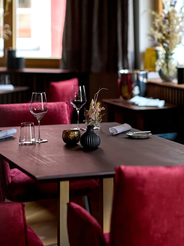 Eleganter Restauranttisch mit roten Samtstühlen, Weingläsern und minimalistischer Deko
